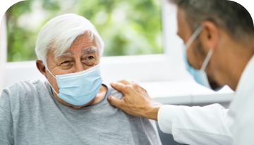 Image of male patient wearing a facemask with a doctor resting a hand on his shoulder