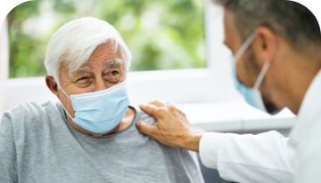 Image of male patient wearing a facemask with a doctor resting a hand on his shoulder